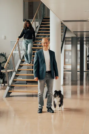 Ein Mann steht mit einem Hund vor einer Treppe, von der gerade eine Frau runterkommt
