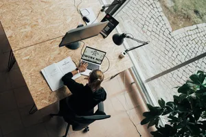 Sicht von oben auf eine Frau, die an einem Arbeitsplatz sitzt und am Laptop arbeitet