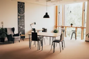 Ein Raum im Coworking Space mit mehreren Tischen, einem Sessel sowie einem Tresen am Fenster mit Blick nach draußen ins Grüne