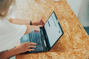 Nahaufnahme eines Laptops auf einem Schreibtisch, auf dessen Bildschirm zwei Personen zeigen.