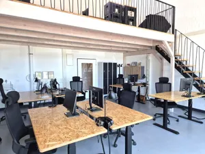 Mehrere Arbeitsplätze im Großraumbüro unter einer offenen Galerie.