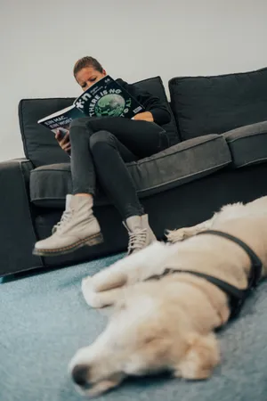 Eine Frau sitzt auf einem Sofa und liest, während vor ihr auf dem Boden ein Hund liegt