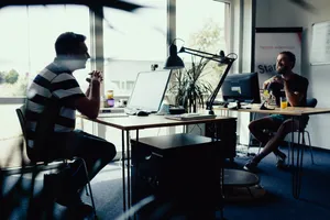 Zwei Männer sitzen sich gegenüber, jeweils an einem Schreibtisch mit Computer